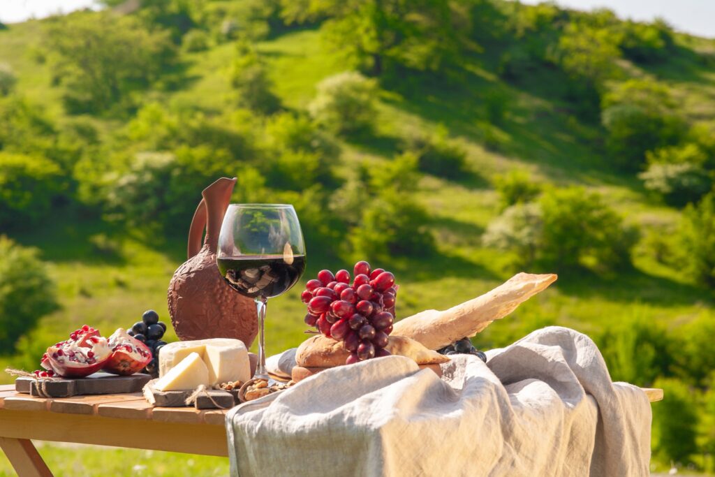 Rustic countryside picnic setup with red wine, cheese, grapes, and a baguette on a wooden table—perfect for vineyard picnics, scenic outdoor lunches, and gourmet food experiences in nature.