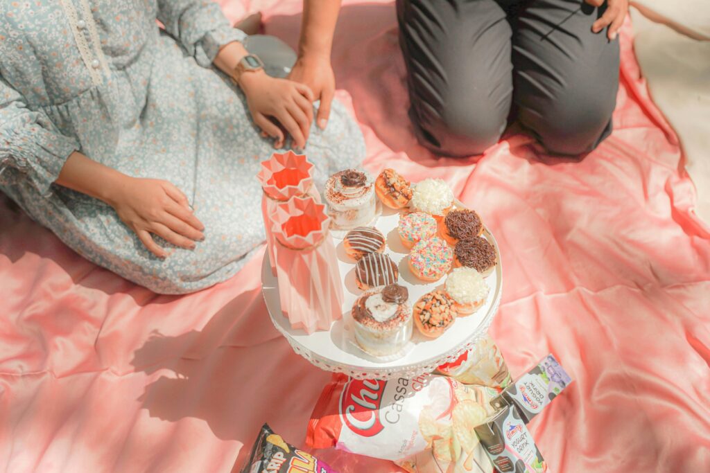 Sweet picnic setup on a pink blanket with assorted donuts, cupcakes, snacks, and refreshing drinks—perfect for casual couple outings, dessert-themed picnics, and fun outdoor dates.
